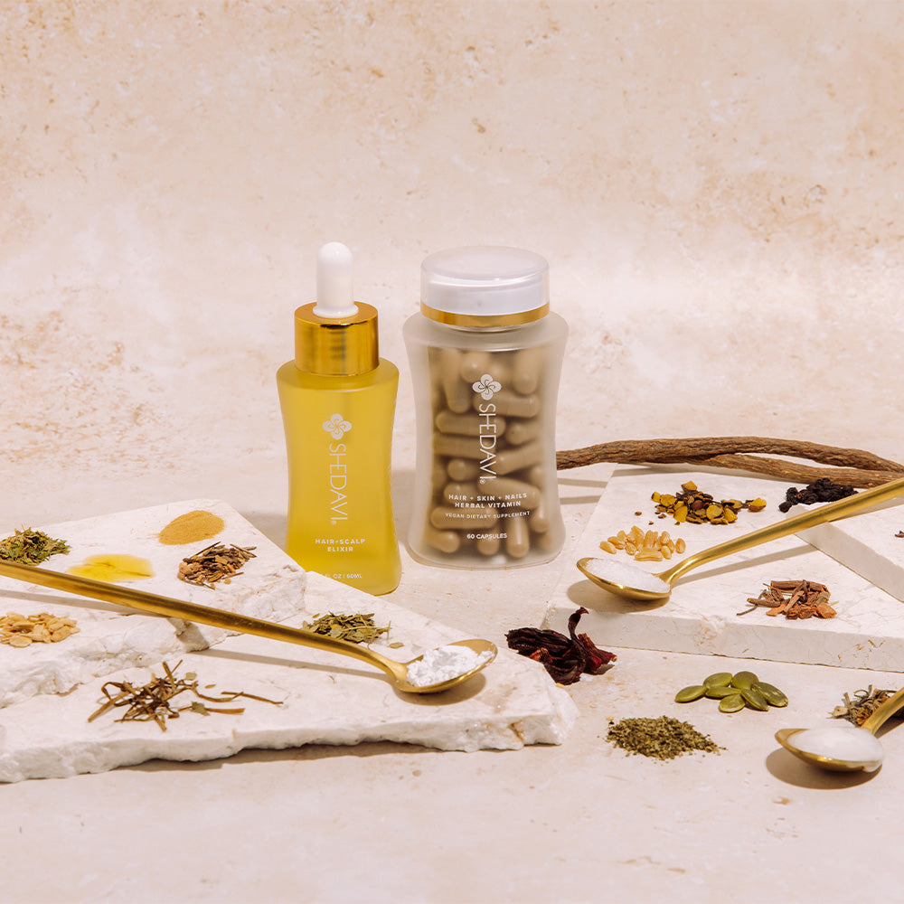 Hair and scalp elixir with herbal vitamin capsules surrounded by various dried herbs and ingredients.